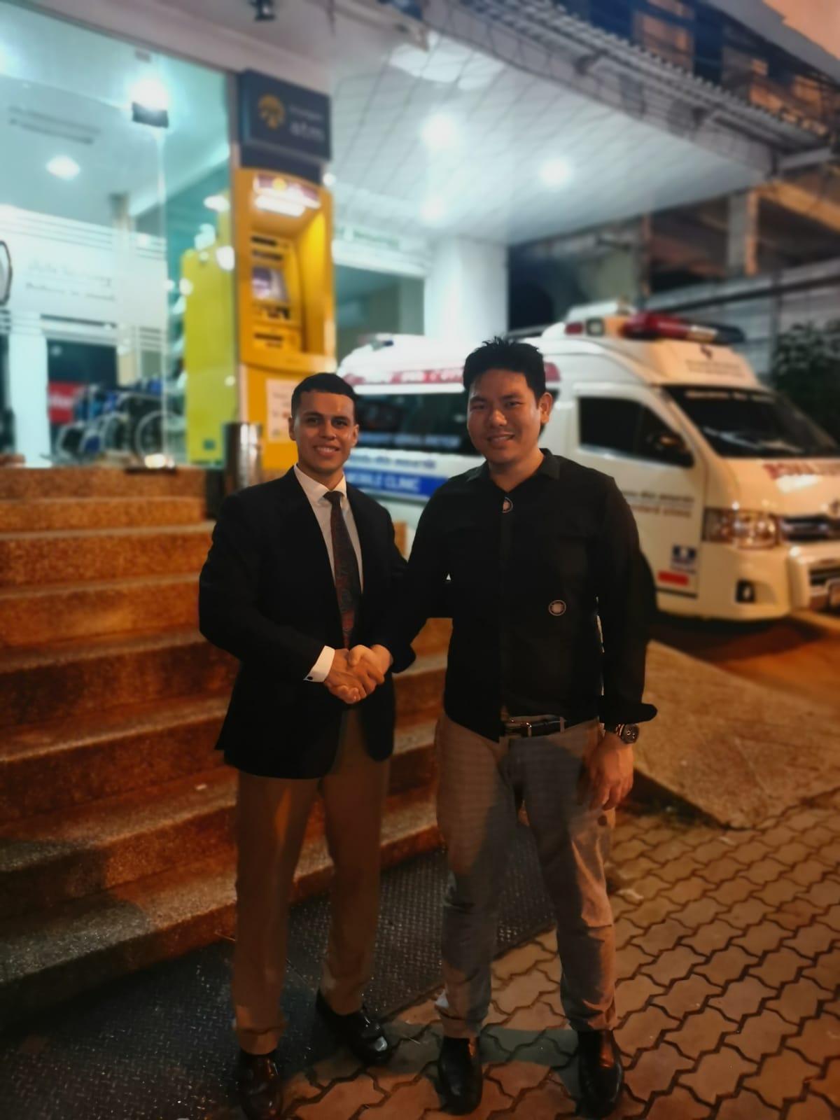 Dr. Yingyong shaking hands with a partner at a medical facility with ambulances